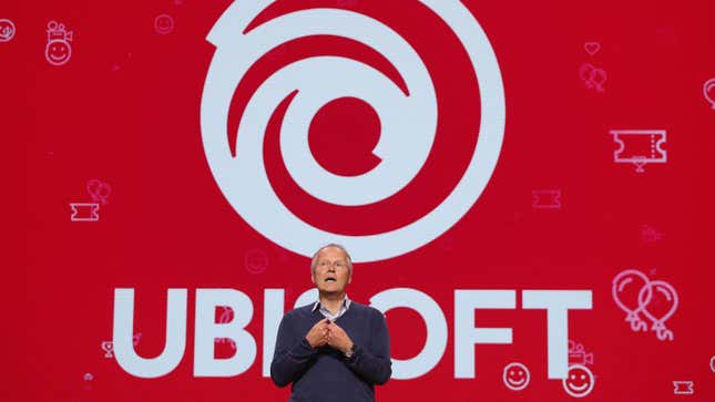 Ubisoft CEO Yves Guillemot stands on stage at E3 2019 in front of a large red background containing the company's logo. 