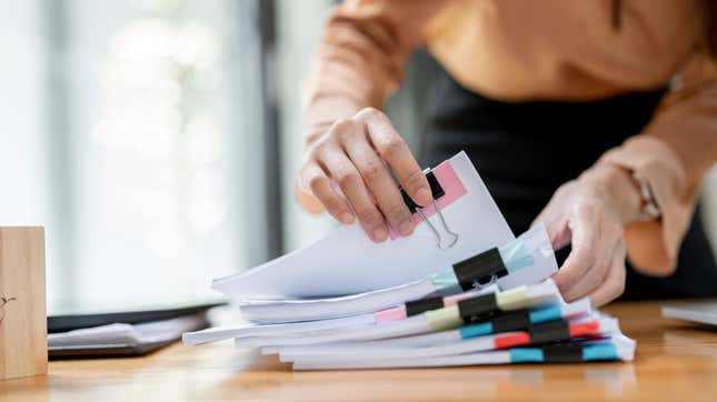 A woman sorts through a stack of documents on a desk, each secured with multi-colored binder clips
