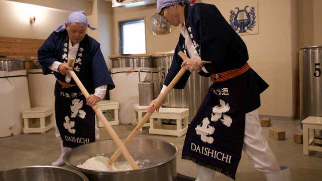 Two brewers use wooden tools to make the yeast starter in a metal tub.