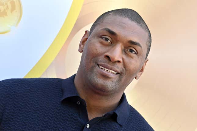 A Black man wearing a blue polo shirt smiles into the camera.