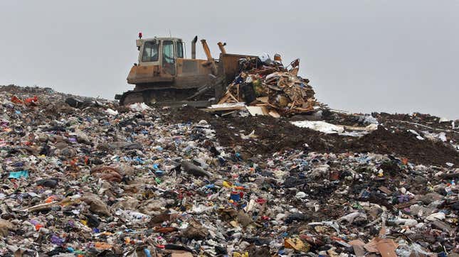 A bulldozer pushes a large pile of trash on top of a landfill hill.
