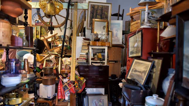 A crowded room filled with jumbled junk, from furniture, to books, to picture frames, to appliances