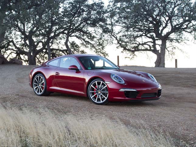 A deep red 2013 Porsche 911 Carrera S is parked on dirt in front of some trees.