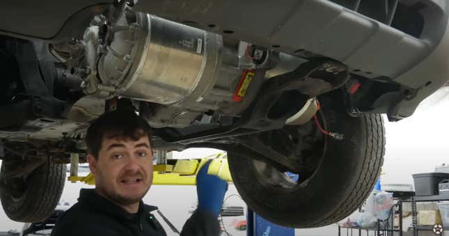 A man points at a Tesla drive unit mounted under a Ford Escape SUV.