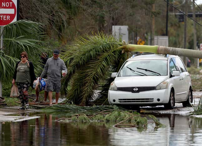People walk past a vehicle that had a palm tree fall on it when Hurricane Ian passed through the area on September 29, 2022 in Fort Myers, Florida.