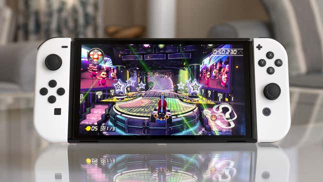 The Nintendo Switch OLED console playing Mario Kart 8 Deluxe sitting on a glass coffee table.