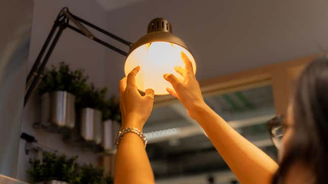 woman changing a lightbulb in a high lamp