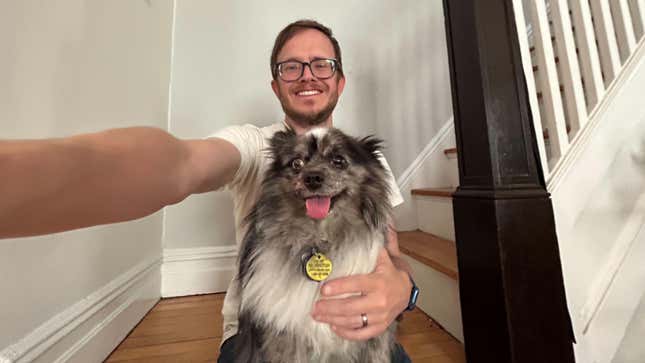 A "0.5 selfie" of a man sitting on stairs with a small grey and white dog on his lap. The skewed perspective makes his arm holding the camera look very long.
