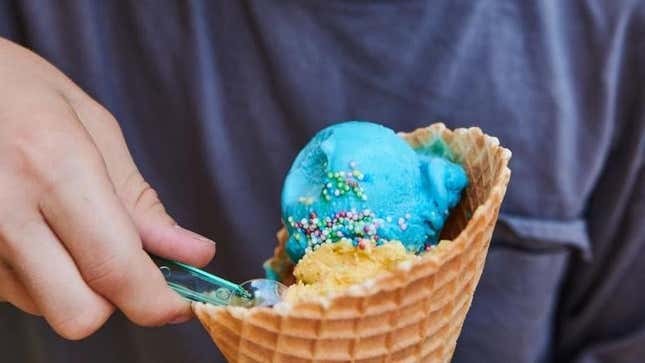 Hand scooping spoon into cone of Blue Moon ice cream