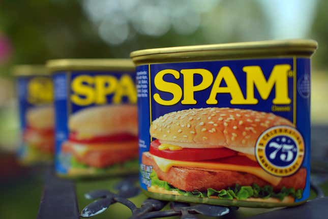 Cans of Spam are shown on a metal table, with those in the background faded out. 