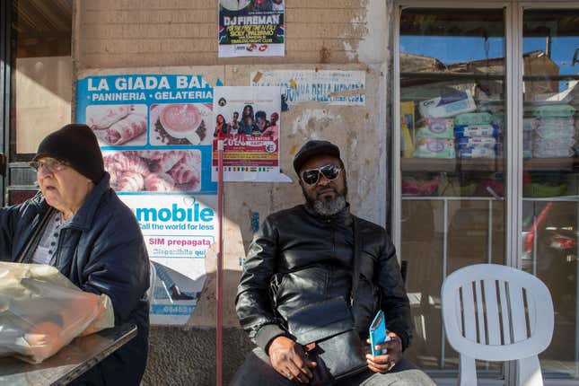 A Nigerian show promoter sits in front of posters advertising shows at a cafe in Palermo.