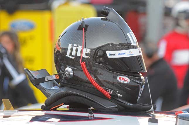 A carbon fiber racing helmet with attached HANS device is placed on top of a race car.
