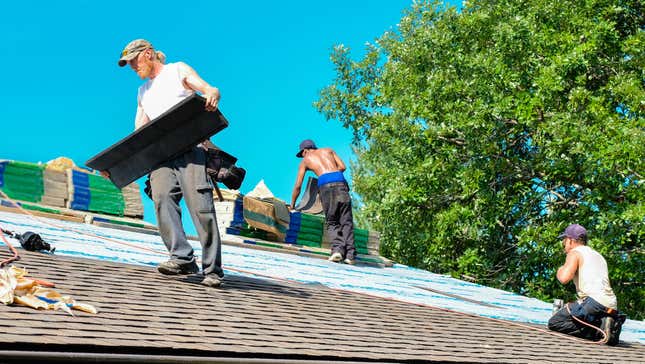 Roofers working on roof on hot summer day; older roofer carrying shingles