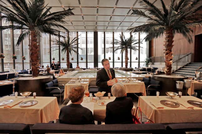 In this July 12, 2016 photo, a waiter speaks with diners in the Pool Room of The Four Seasons, in New York's landmarked Seagram building, which has housed the restaurant for 57 years. Designed by the legendary architect Philip Johnson and the building's architect Ludwig Mies van der Rohe, the restaurant was a favorite of celebrities and business titans ever since it opened in 1959. The epitome of the midcentury style in Midtown Manhattan, The Four Seasons is scheduled to close on Saturday, July 16. (AP Photo/Richard Drew)