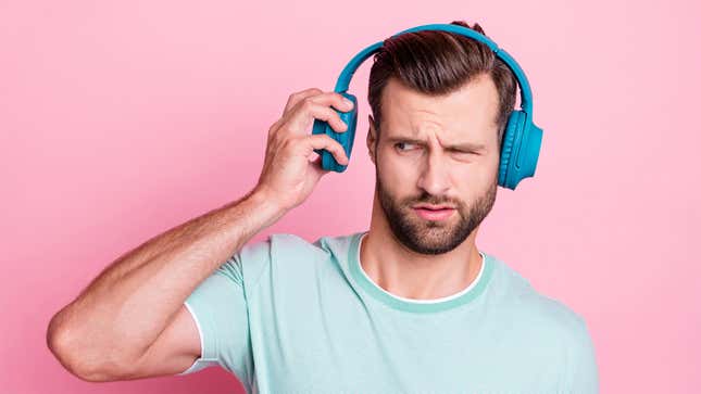 A man pulls headphones from his head with an awkward look on his face.