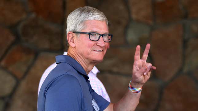 Apple CEO Tim Cook wearing a blue polo shirt walks by and makes the "peace sign" of to fingers held up to the camera.