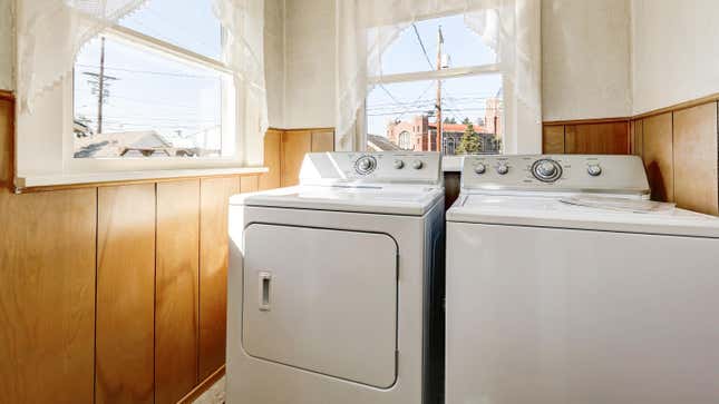 AN older wood-paneled laundry room containing older models of white washer and dryer