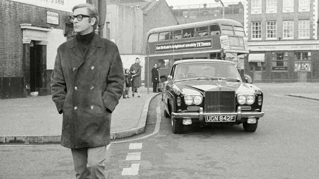 A black and white photo of Michael Caine walking around London. 