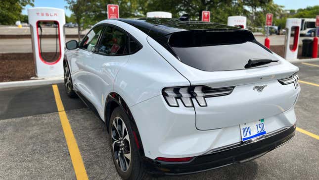 A white Ford Mustang Mach-E parking in front of a Tesla Supercharger.