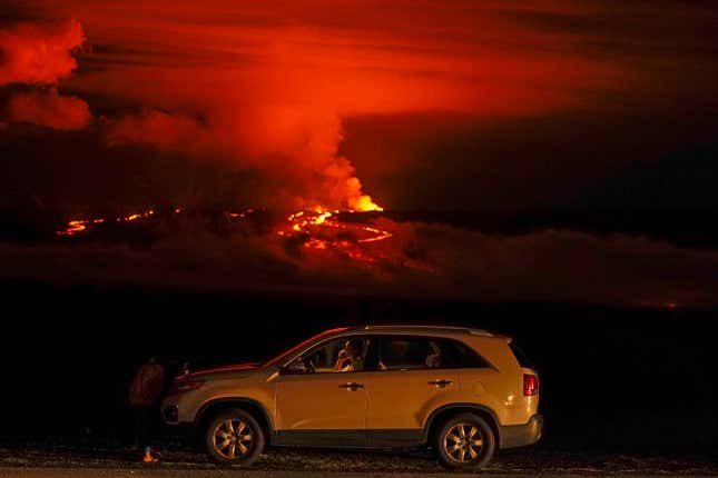 A man talks on a phone in his car alongside Saddle Road as the Mauna Loa volcano erupts Wednesday, Nov. 30, 2022, near Hilo, Hawaii.