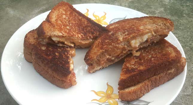 Four peanut butter banana bacon sandwich triangles fried golden brown and stacked on a plate