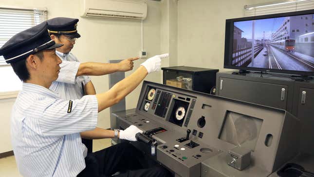 Two men in train station outfits operate the simulator. 