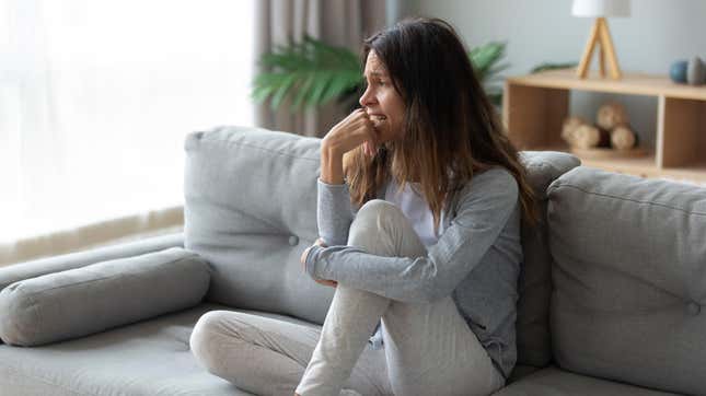 A woman sites on a couch looking sad