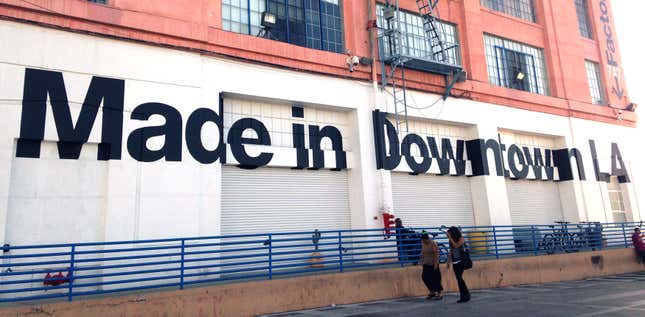 Two people walk past the American apparel factory building and outlet store in Los Angeles, California July 7, 2014. Ousted American Apparel Inc head Dov Charney supported workers in the clothing industry with his stance in favor of immigration rights and determination to keep jobs in the United States, but some employees are not returning the favor. Last month American Apparel's board dismissed Charney. It accused the chairman, president and chief executive of misusing corporate funds and failing to prevent the dissemination of nude photos of a female ex-employee who sued him. Picture taken July 7, 2014. To match Feature AMERICAN-APPAREL-WORKERS/ REUTERS/Lisa Baertlein (UNITED STATES - Tags: BUSINESS EMPLOYMENT SOCIETY CRIME LAW) - RTR3XO82
