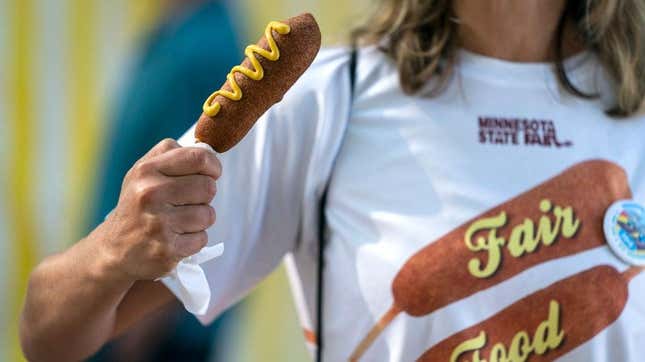 Woman holding corn dog wearing shirt that reads "Fair Food"