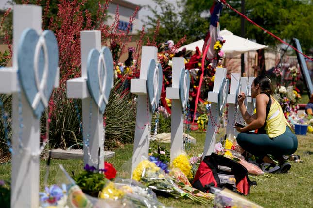 A woman signs a cross that stands by others at a makeshift memorial for the victims of a mass shooting, Monday, May 8, 2023, in Allen, Texas. 