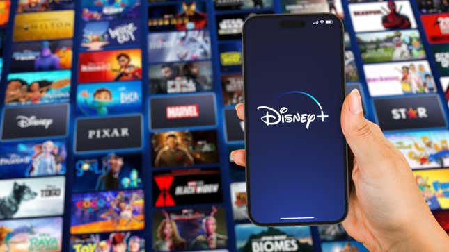 A person holding a phone with the Disney+ logo in front of a screen of several disney products like pixar and marvel