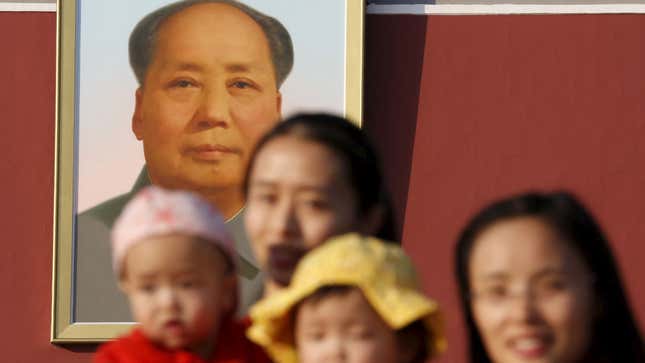 Two women and their babies pose in front of a portrait of Chairman Mao