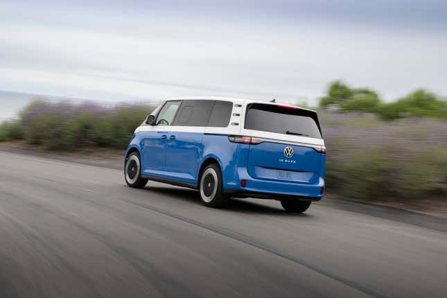 A blue and white VW ID Buzz electric van drives on a California road, rear-three-quarter view