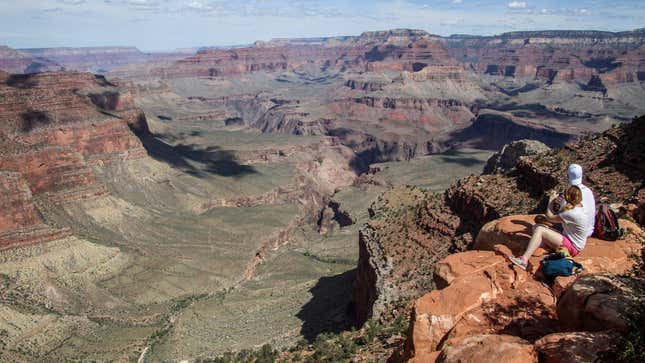 Hikers sit by the edge of the cliffs of the Grand Canyon.