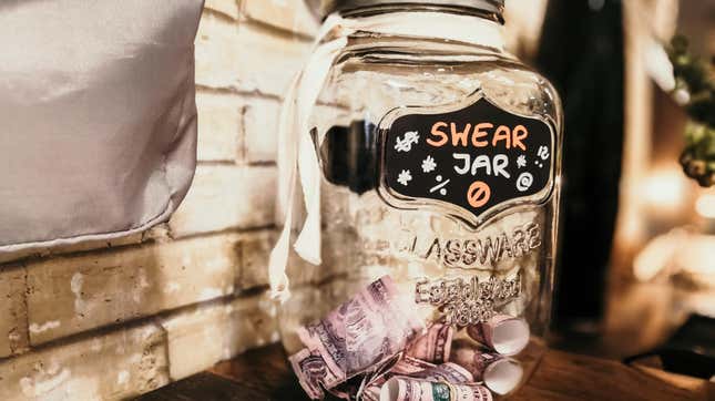 A jar with money sitting inside it with the words swear jar on its outside.