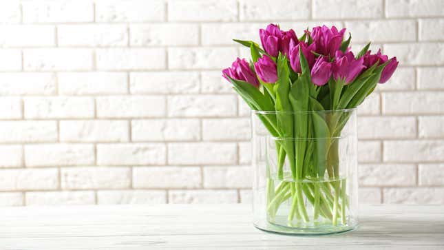 A bouquet of tulips in a clear glass vase on a white countertop against a painted white brick wall