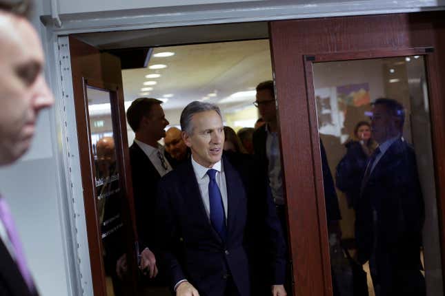 Howard Schultz walks through a doorway at Purdue University wearing a suit and blue tie.