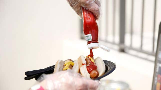 Gloved hands dispense ketchup onto hot dog