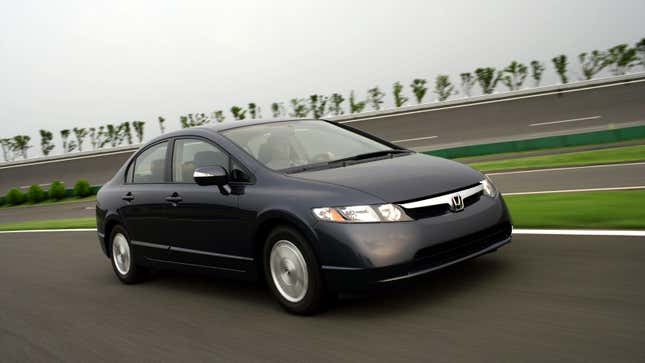 A photo of a dark grey Honda Civic sedan driving on a road. 