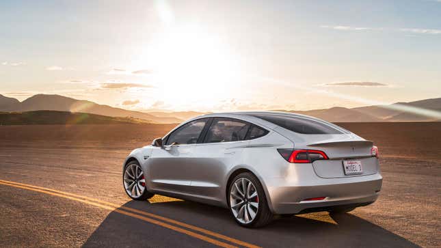 A photo of a silver Tesla Model 3 sedan parked on a desert road. 