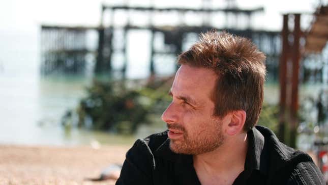Ken Levine, staring to his left, in front of a blurred seaside pier.