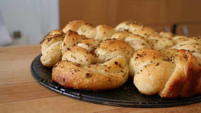 Tray of golden brown garlic knots topped with herb seasonings