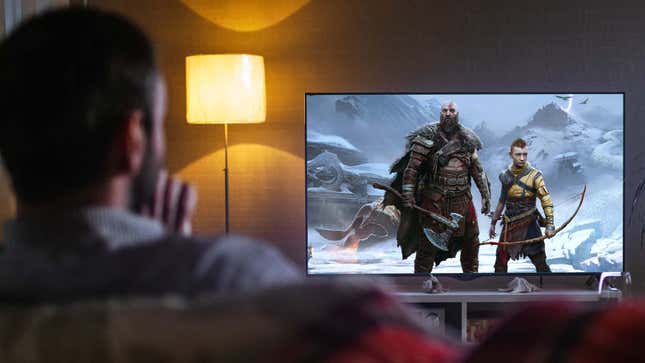 A man watches a TV with Kratos and Atreus on the screen. 
