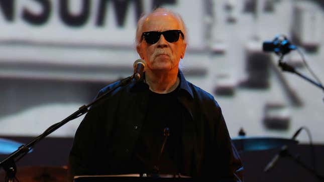 John Carpenter wearing sunglasses during a live screening of his famous "They Live" film. 