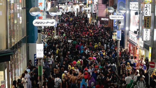 Crowds of people wearing costumes fill a Tokyo street.