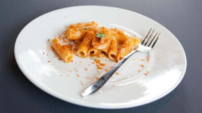 Half-eaten plate of pasta with tomato sauce with a fork