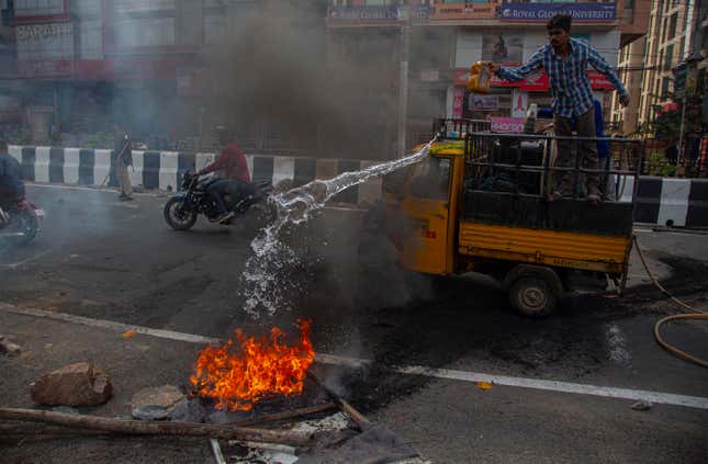 Police clear road blocks as a man tries to douse a fire set by protestors in Gauhati, India on Dec. 12.