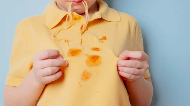 Young child eating spaghetti, gets pasta stain on his shirt.