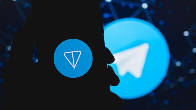 A silhouette of a hand holding a phone with the TON coin logo on it in front of a Telegram messaging app logo.