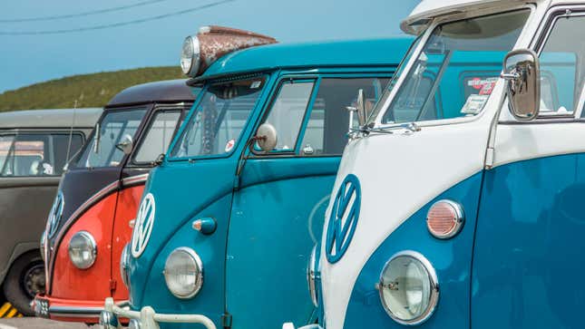 A row of four brightly colored VW buses at a meetup. 